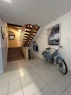 Una escalera con barandilla de madera que conduce a una plataforma, una bicicleta fijada a la pared y un cuadro enmarcado.