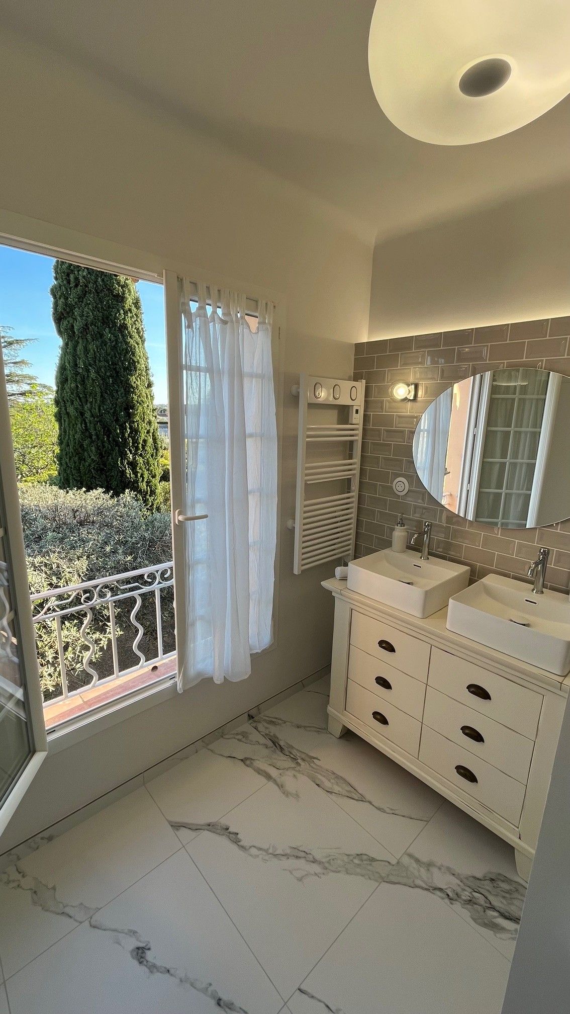 A bathroom with a large window, a mirror, two sinks, and a towel rack.