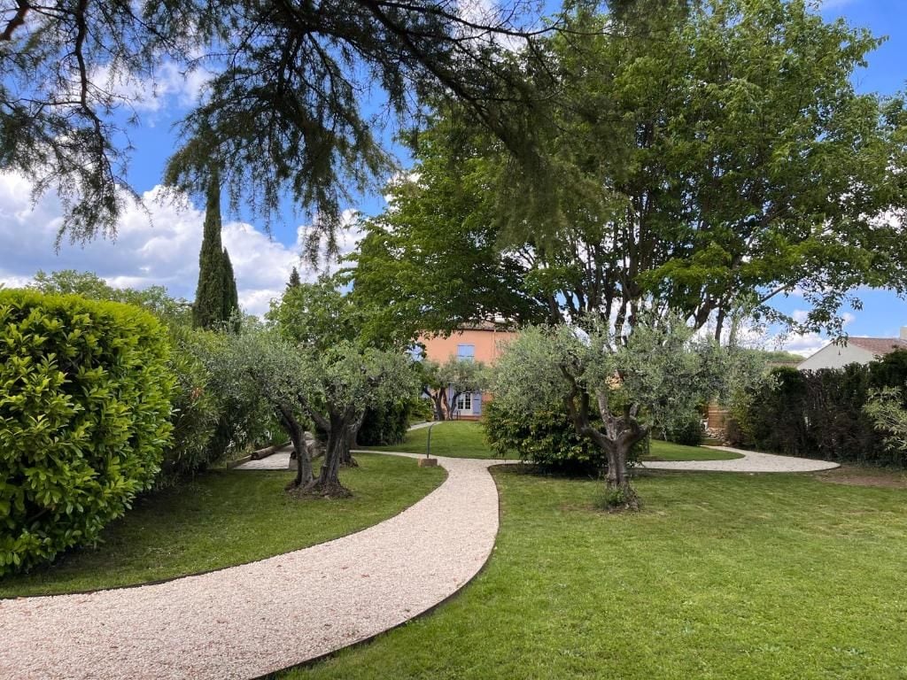 A garden with a gravel path, various trees, and a building in the background.