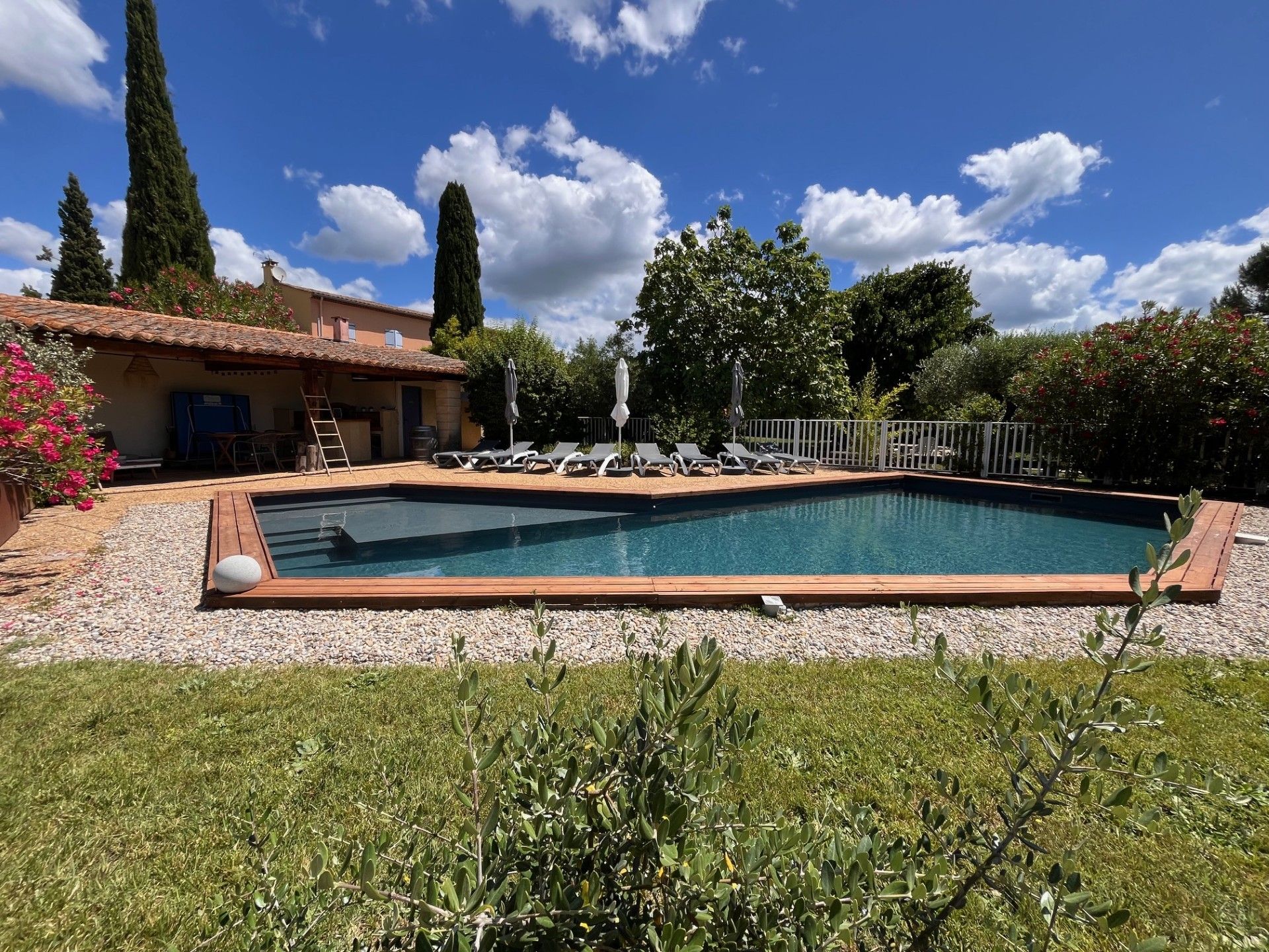 A rectangular swimming pool with a wooden deck, surrounded by a gravel area and grass.