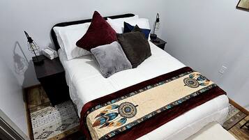 A neatly made bed with a patterned throw, a bedside table with a lamp, and a wall with framed pictures.