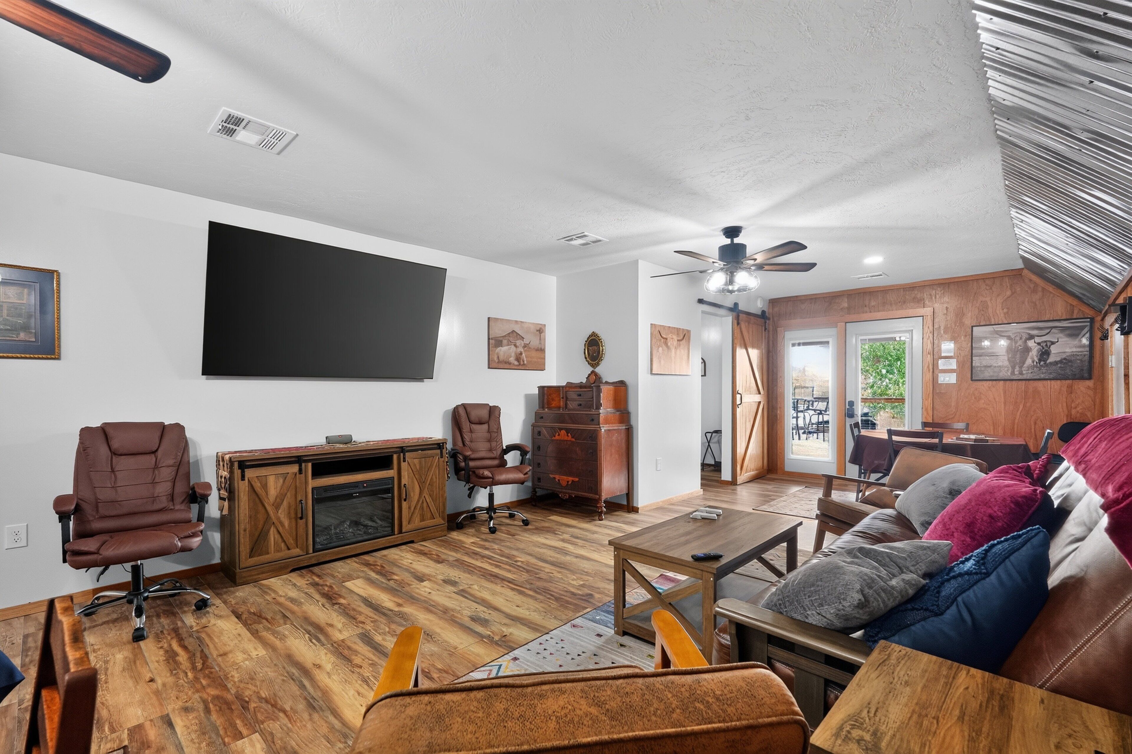 A living room with a fireplace, a ceiling fan, and a large flat-screen TV mounted on the wall.