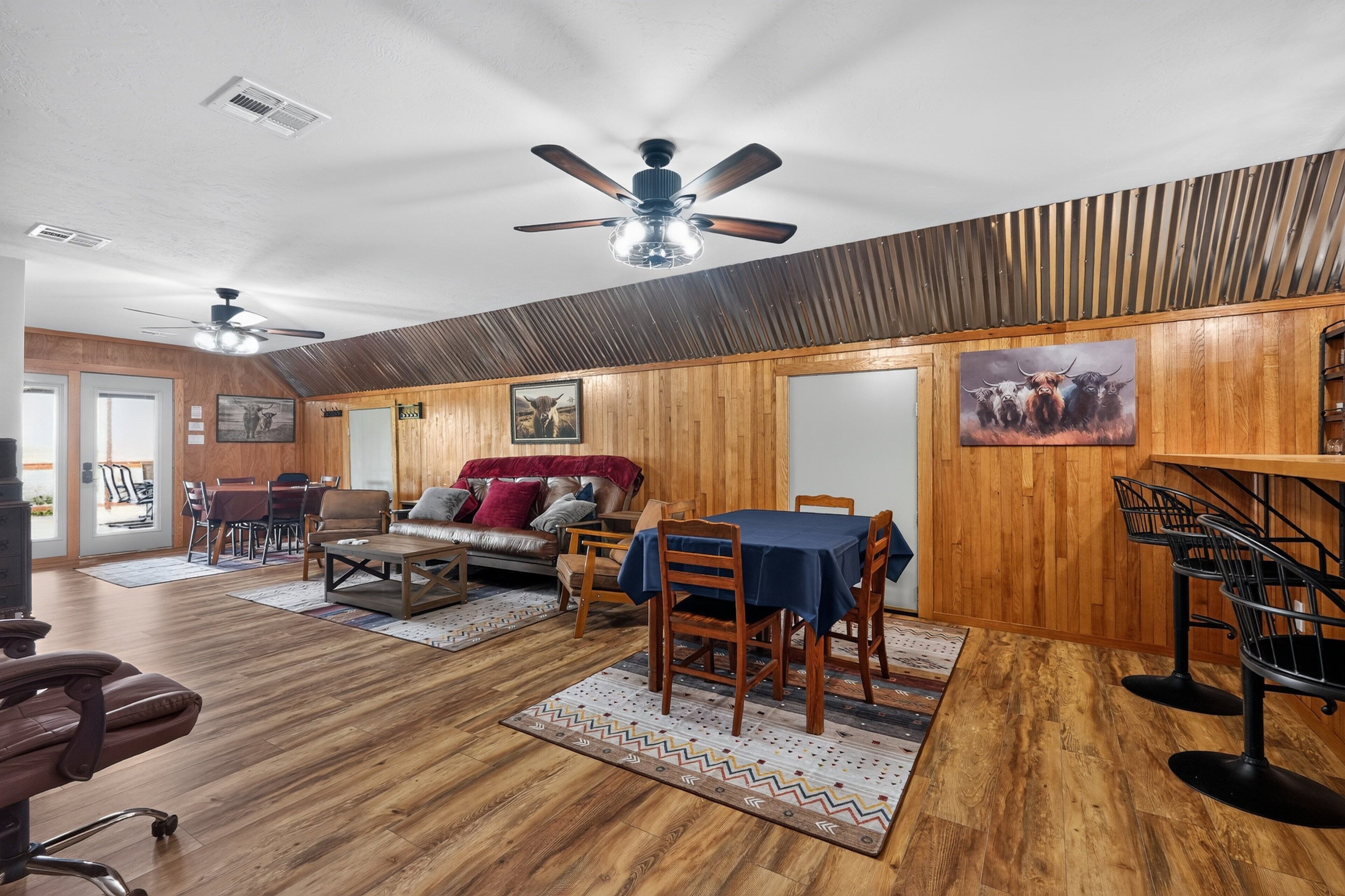 Une pièce spacieuse avec un plafond haut, des murs en bois, un coin repas avec une table et des chaises, et un canapé.