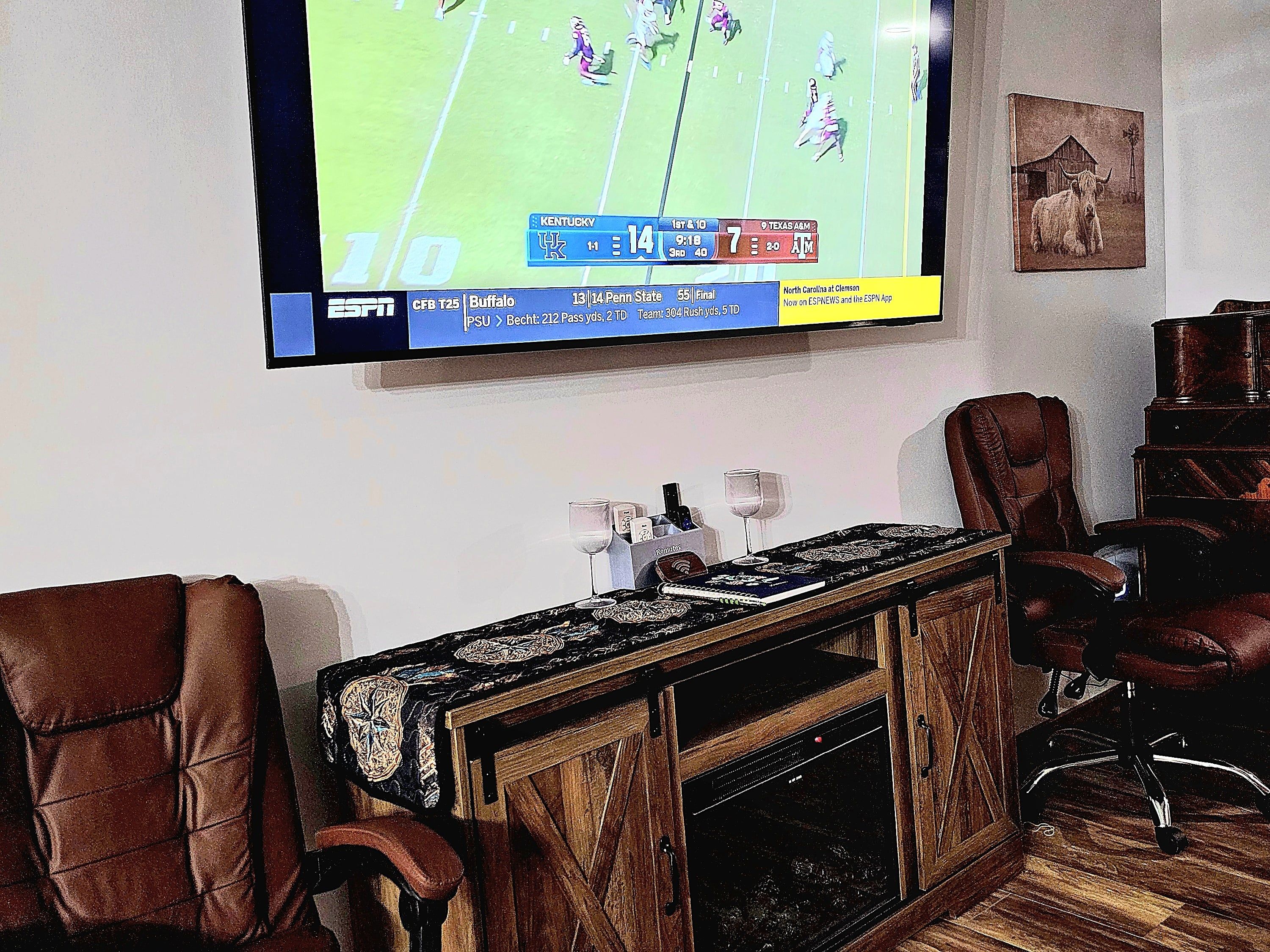 A living room with a flat-screen TV mounted on the wall, a wooden entertainment center, leather armchairs, and a fireplace.