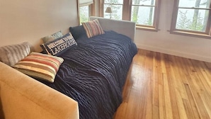 A bedroom with a bed, a wooden floor, and three windows with blinds.