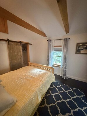 Une chambre à coucher avec un lit, une fenêtre avec des rideaux, un plafond en bois et une étagère fixée au mur.