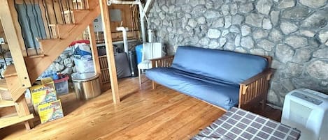 A cozy cabin interior with a wooden staircase, a stone wall, a blue sofa, and a plaid bedspread.