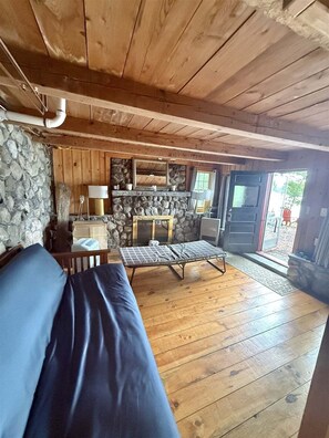 Interior acolhedor de uma cabana com parede de pedra, teto de madeira, um sofá, um banco e uma lareira.