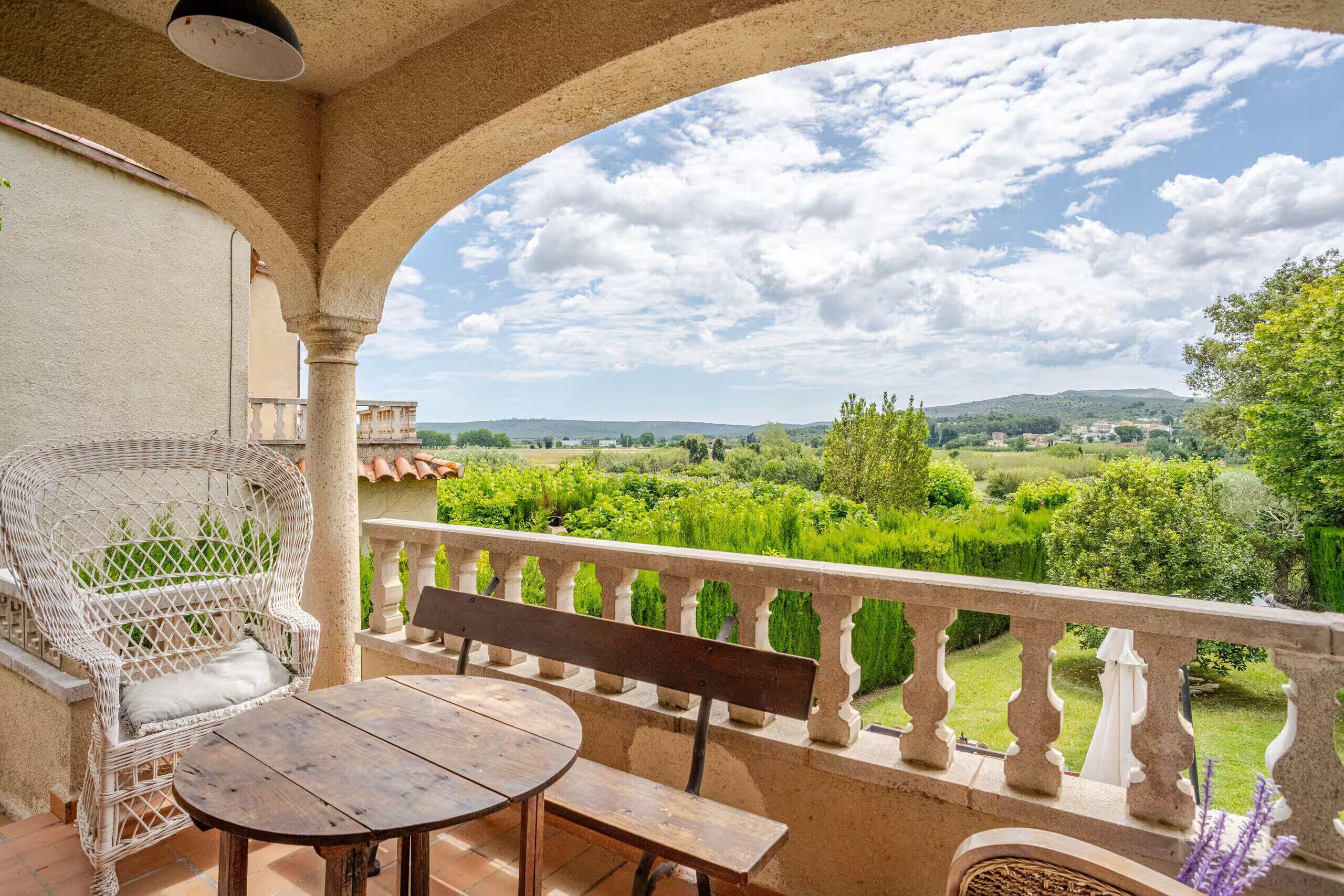 Ein Balkon mit Blick auf eine grüne Landschaft, ein Korbstuhl und ein Holztisch.