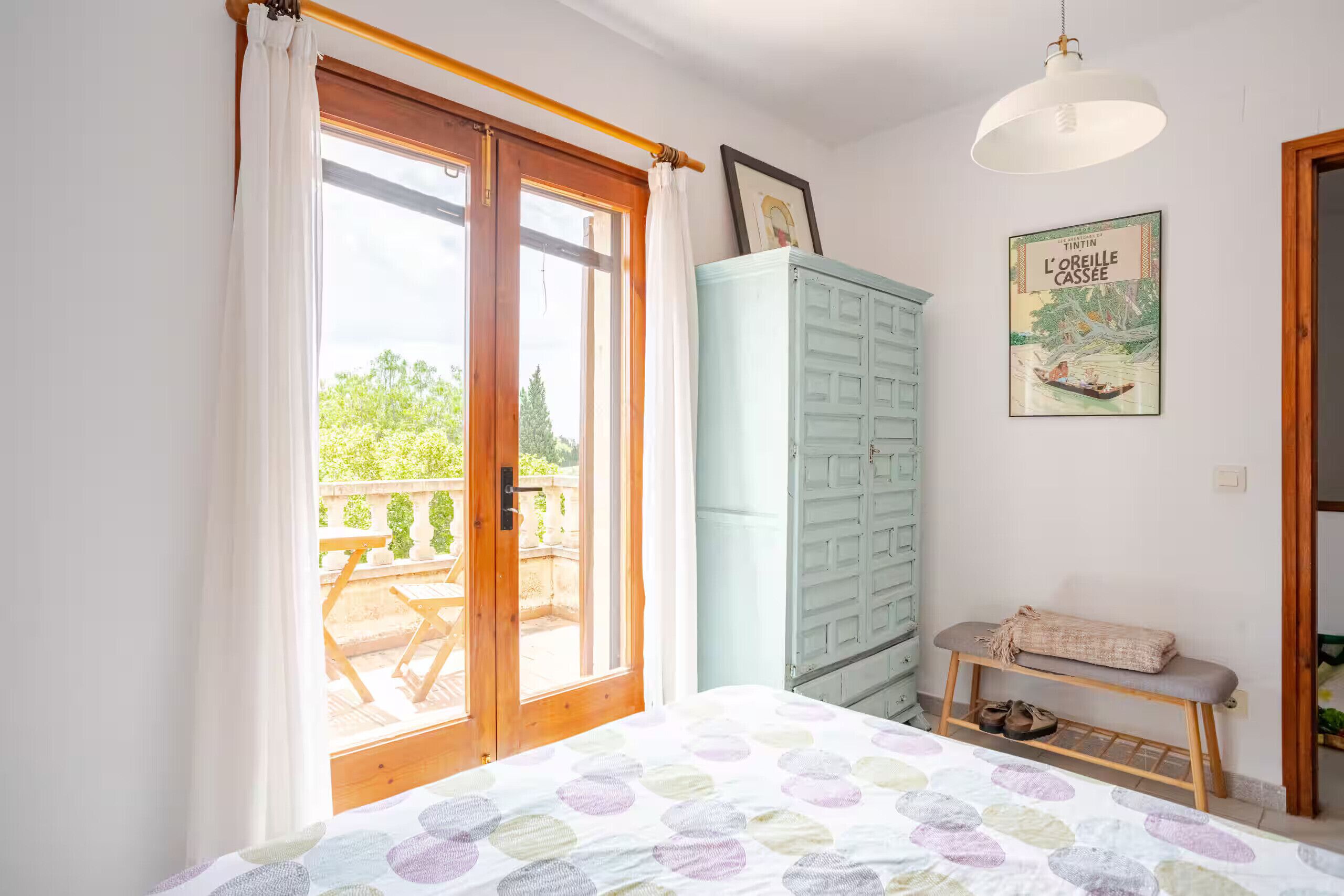 Een slaapkamer met een bed, een bankje, een kledingkast en een raam met gordijnen.