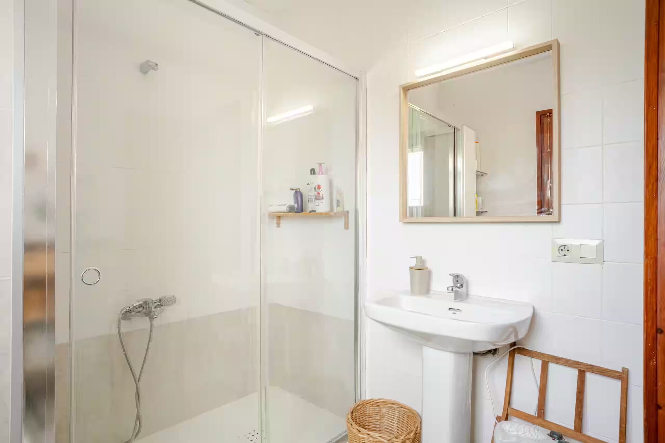 Une salle de bain avec une douche à parois de verre, un lavabo blanc et un miroir au mur.