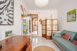 Ein Wohnzimmer mit einem Holzespeisetisch, einem grünen Sofa mit Kissen mit amerikanischer Flagge, einer weißen Kommode mit Glastüren und einem Baumgemälde an der Wand.