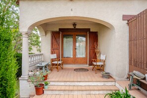 A covered porch with two wooden chairs, a small table, and potted plants.