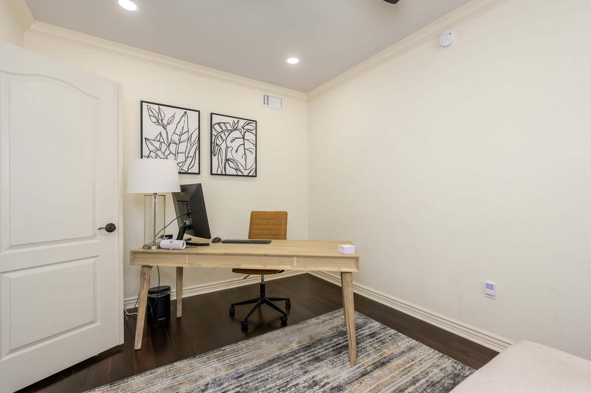 A room with a desk, chair, lamp, and two wall art pieces.
