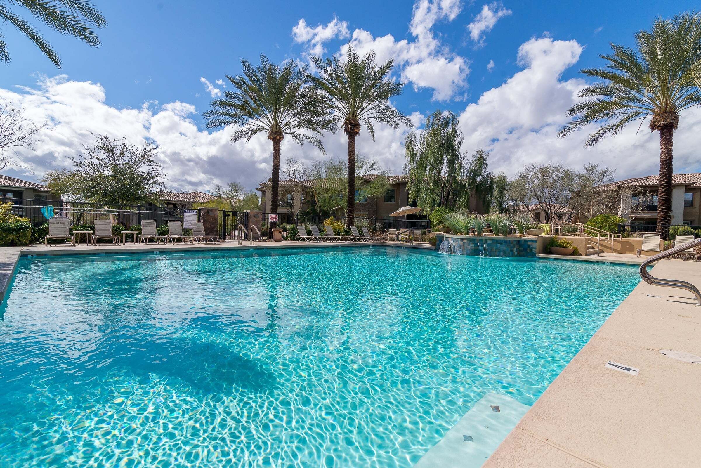 A clear blue pool with lounge chairs and palm trees.