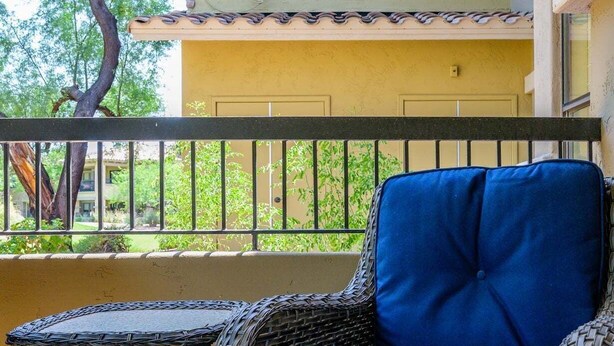 A wicker chair with a cushion and a small table on a balcony with a railing. - Villa Bella Monte 1 Bedroom Condo (Phoenix)