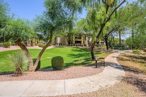 A landscaped outdoor area with a pathway, neatly trimmed grass, and a variety of trees. - Villa Bella Monte 1 Bedroom Condo (Phoenix)