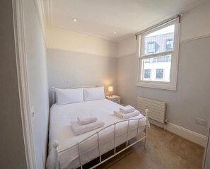 Ein Schlafzimmer mit Bett, Nachttisch, Lampe und Fenster.