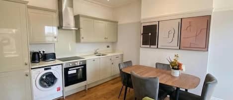 A modern kitchen with built-in appliances, a dining area with a table and chairs, and a green sofa.