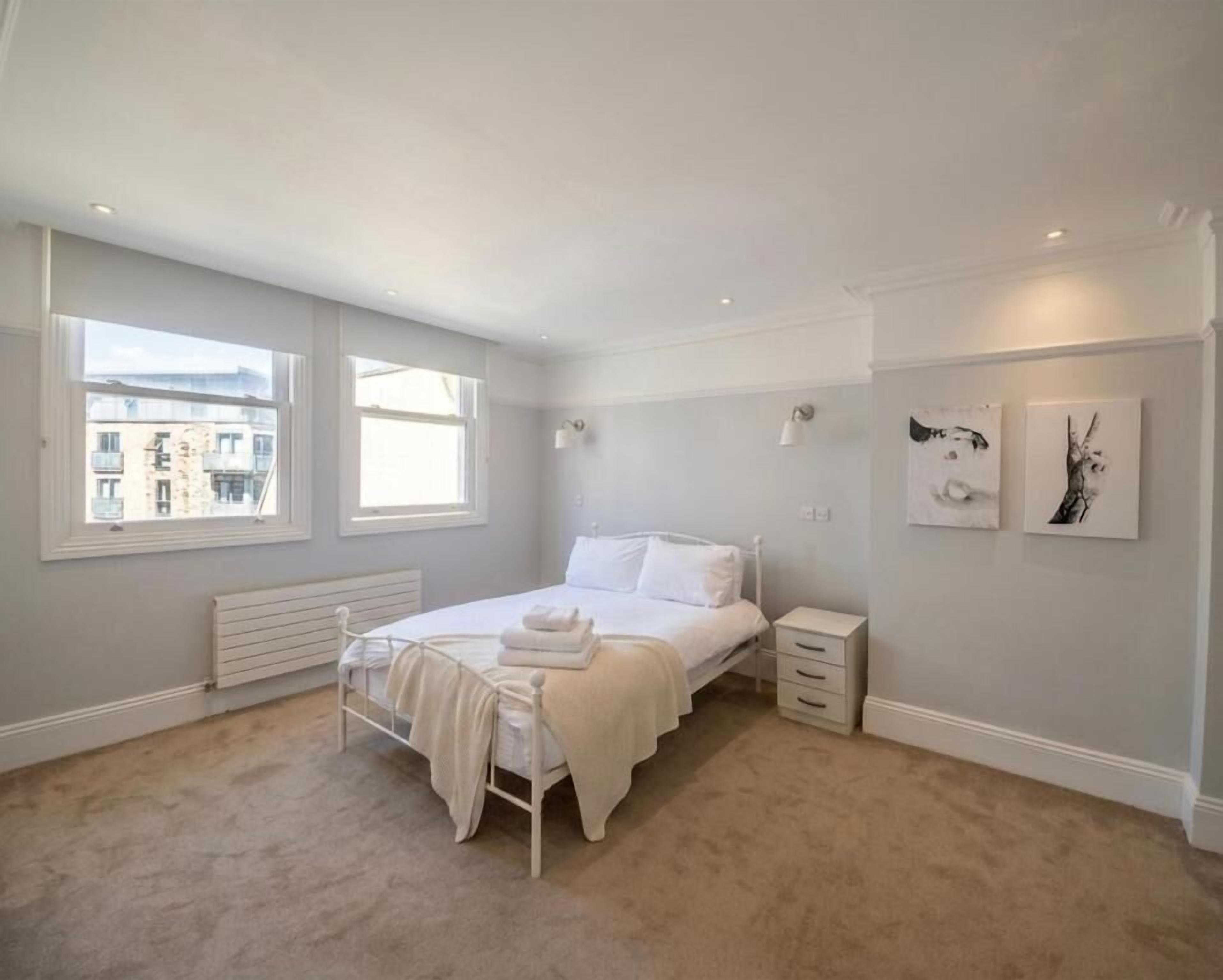 A bedroom with a bed, bedside tables, a radiator, and artwork on the walls.