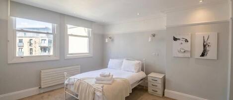 A bedroom with a bed, bedside tables, a radiator, and artwork on the walls.