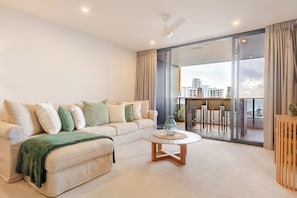 A modern living room with a sofa, a coffee table, and a view of a cityscape through large windows. - Modern living, prime location, everything within easy reach - Broadbeach stay. (Broadbeach)