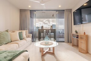 Uma sala de estar moderna com sofá, mesa de centro, televisão e varanda com vista para a cidade.