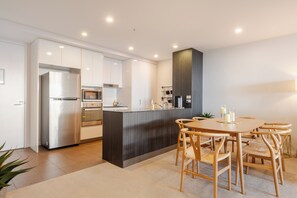 A modern kitchen with stainless steel appliances, a dark wood island, and a dining area with wooden chairs. - Modern living, prime location, everything within easy reach - Broadbeach stay. (Broadbeach)