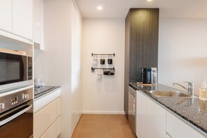 Uma cozinha moderna com eletrodomésticos de aço inoxidável, bancada de granito e um suporte para panelas suspenso.