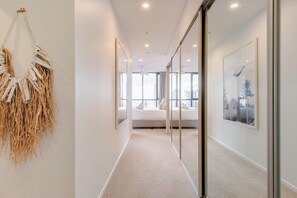 Um corredor que leva a um quarto com uma cama, uma janela grande e um quadro na parede.