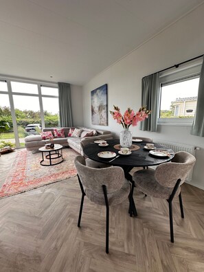A modern living room with a dining area, large windows, and a view of the outside.