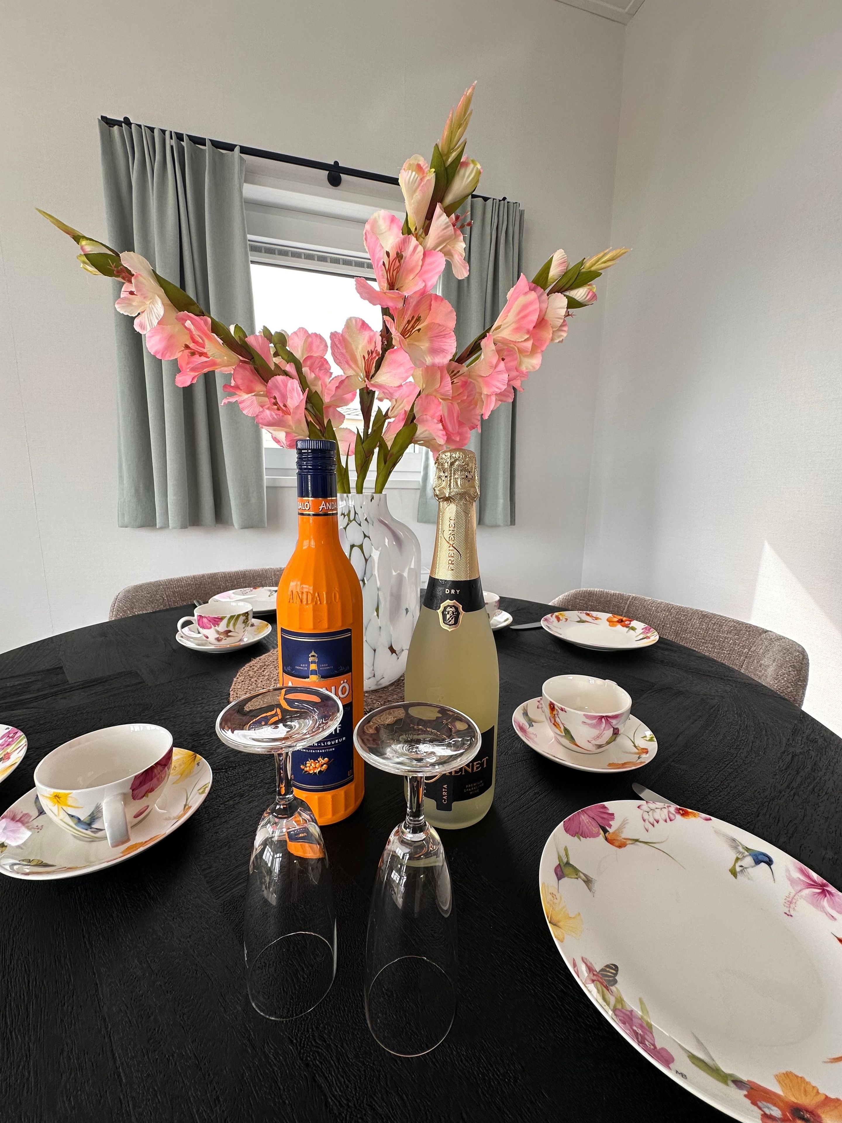 Une table à manger avec de la vaisselle à motifs floraux, deux bouteilles de vin et deux verres à vin.