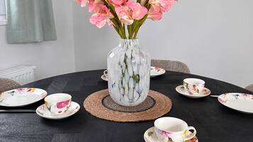 Een ronde eettafel met borden met bloemenprint, een vaas met roze bloemen en een klok aan de muur.