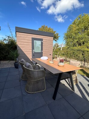 A small wooden structure with a door and window, surrounded by outdoor furniture and plants. - Chalet 'Arcabo Beachhouse' with Private Terrace, Garden, and WiFi (Scharendijke)