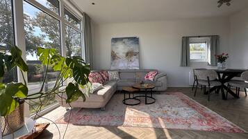 Ein modernes Wohnzimmer mit großem Fenster, einem grauen Sofa, einem Couchtisch und einem Essbereich mit Stühlen.