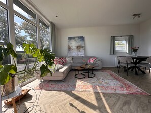 A modern living room with a large window, a grey sofa, a coffee table, and a dining area with chairs.