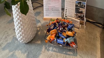 Een witte, gestructureerde vaas met een rode roos, een folderhouder en een schaal met diverse chocolades.