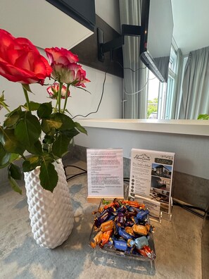 A white textured vase with a red rose, a brochure stand, and a tray of assorted chocolates.