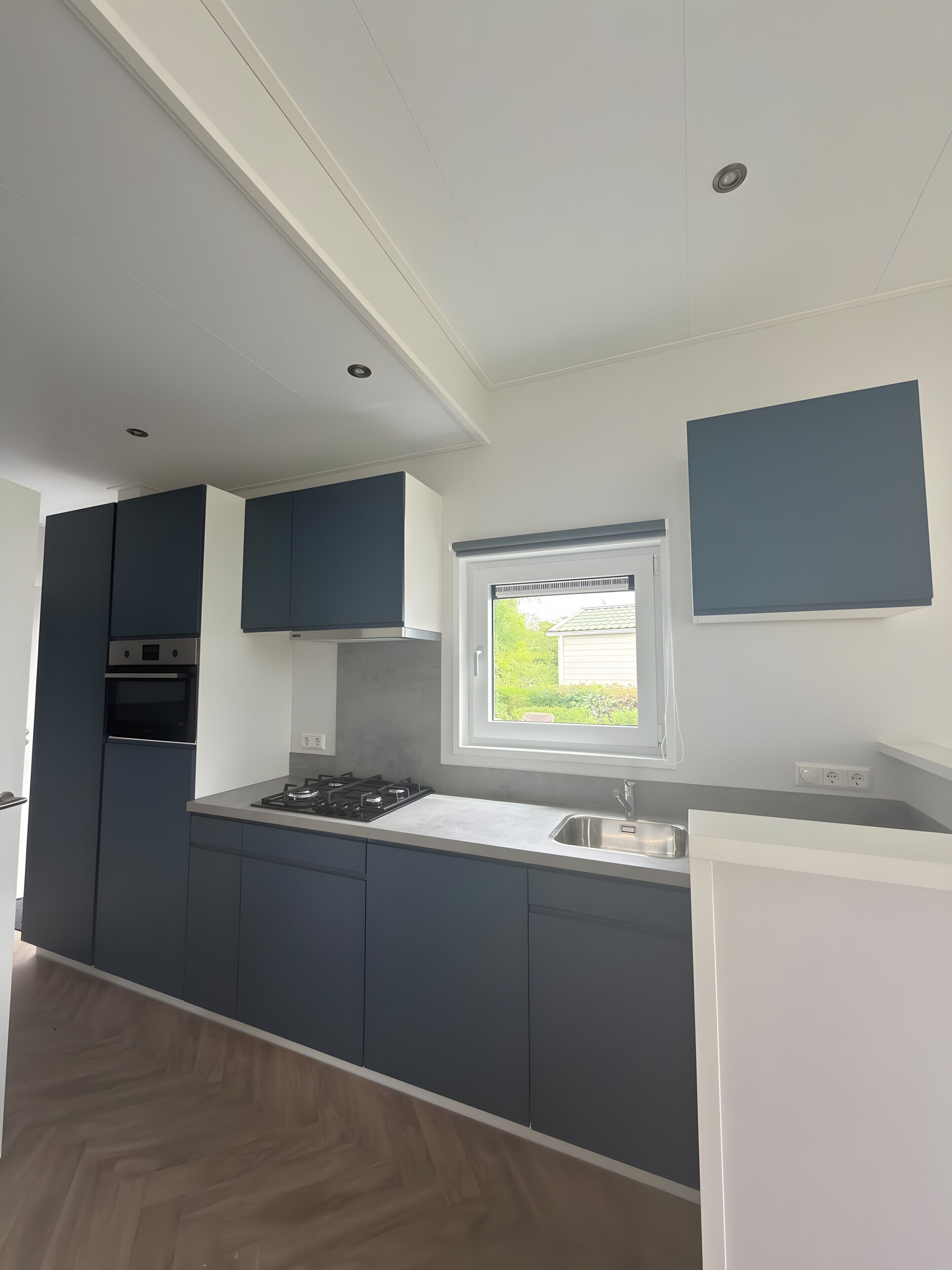 A modern kitchen with built-in appliances, a window with a view, and a white countertop.