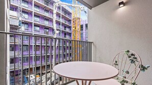 A balcony with a table and chairs, overlooking a construction site with a purple building and a yellow crane. - #20 LuxDigbeth Apt|near Hippodrome Square|Sleeps 6 (Deritend)