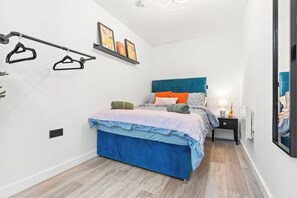 A bedroom with a bed, a bedside table, a nightstand, a wall-mounted rack, and a shelf with framed pictures. - #20 LuxDigbeth Apt|near Hippodrome Square|Sleeps 6 (Deritend)