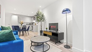 A modern living room with a blue sofa, a coffee table, a TV on a black stand, and a floor lamp. - #20 LuxDigbeth Apt|near Hippodrome Square|Sleeps 6 (Deritend)