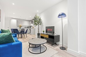 A modern living room with a blue sofa, a coffee table, a TV on a black stand, and a floor lamp. - #20 LuxDigbeth Apt|near Hippodrome Square|Sleeps 6 (Deritend)