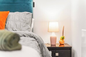 A neatly made bed with a grey comforter and pillows, a teal headboard, a bedside lamp, and a small orange decorative item on the nightstand. - #20 LuxDigbeth Apt|near Hippodrome Square|Sleeps 6 (Deritend)