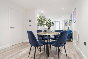 A modern dining area with a round table, blue chairs, and potted plants. - #20 LuxDigbeth Apt|near Hippodrome Square|Sleeps 6 (Deritend)