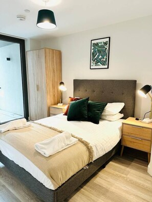 Ein modernes Schlafzimmer mit einem großen Bett, Nachttischlampen, einem Holzschrank und einem gerahmten Kunstwerk an der Wand.