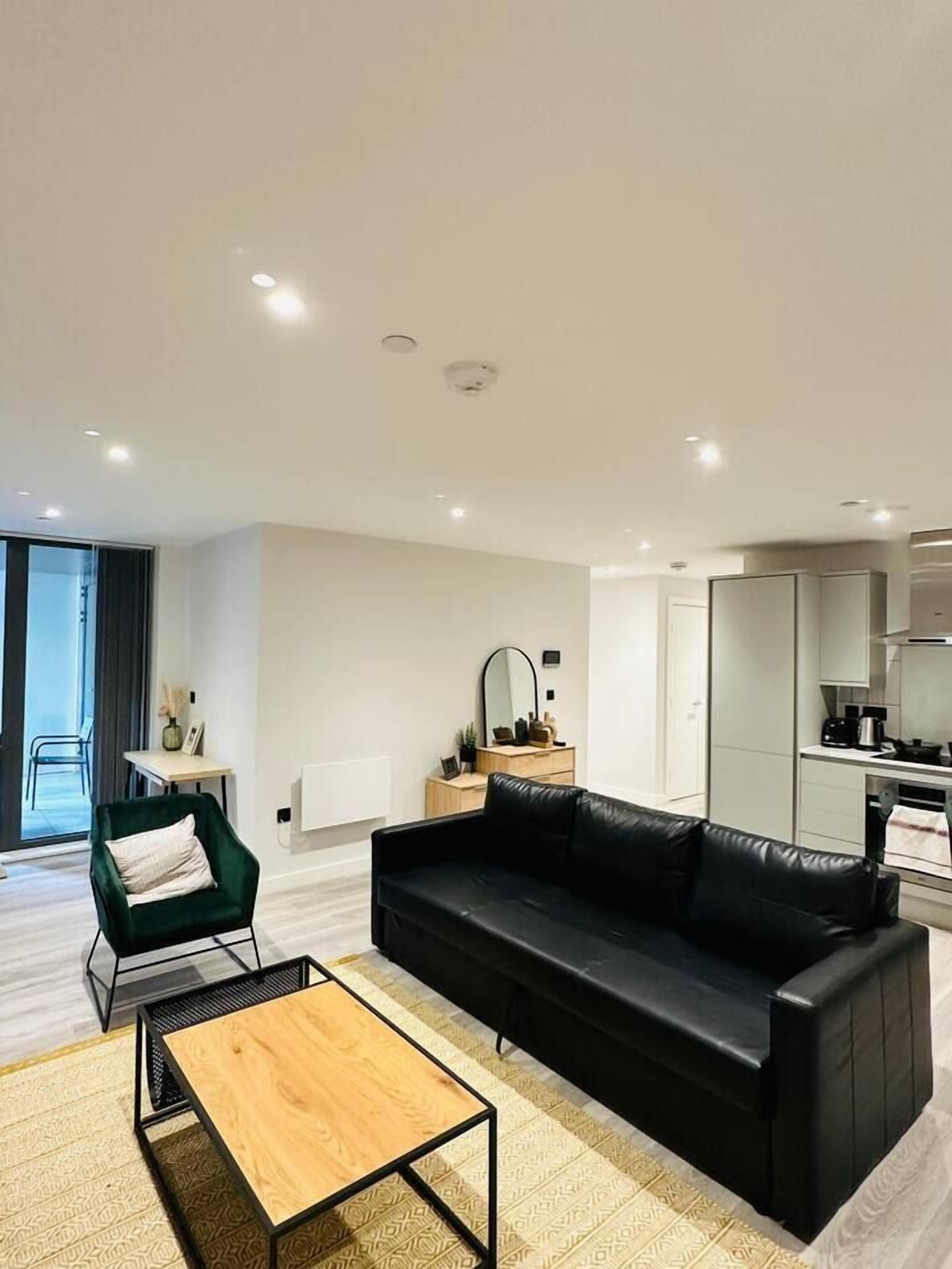 A modern living room with a black sofa, a wooden coffee table, and a green armchair.