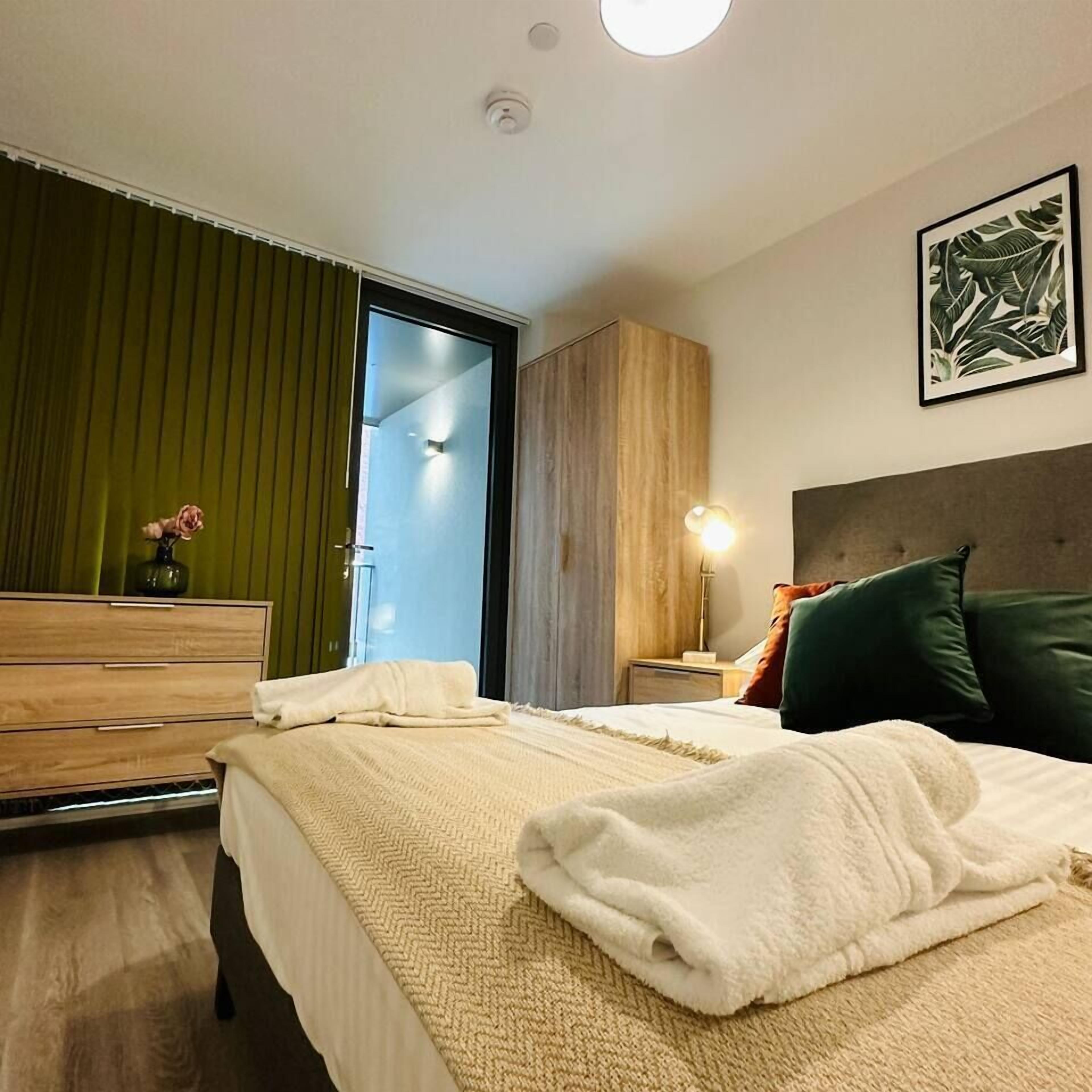 A hotel room with a bed, a dresser, a nightstand, a lamp, a painting, and a green curtain.