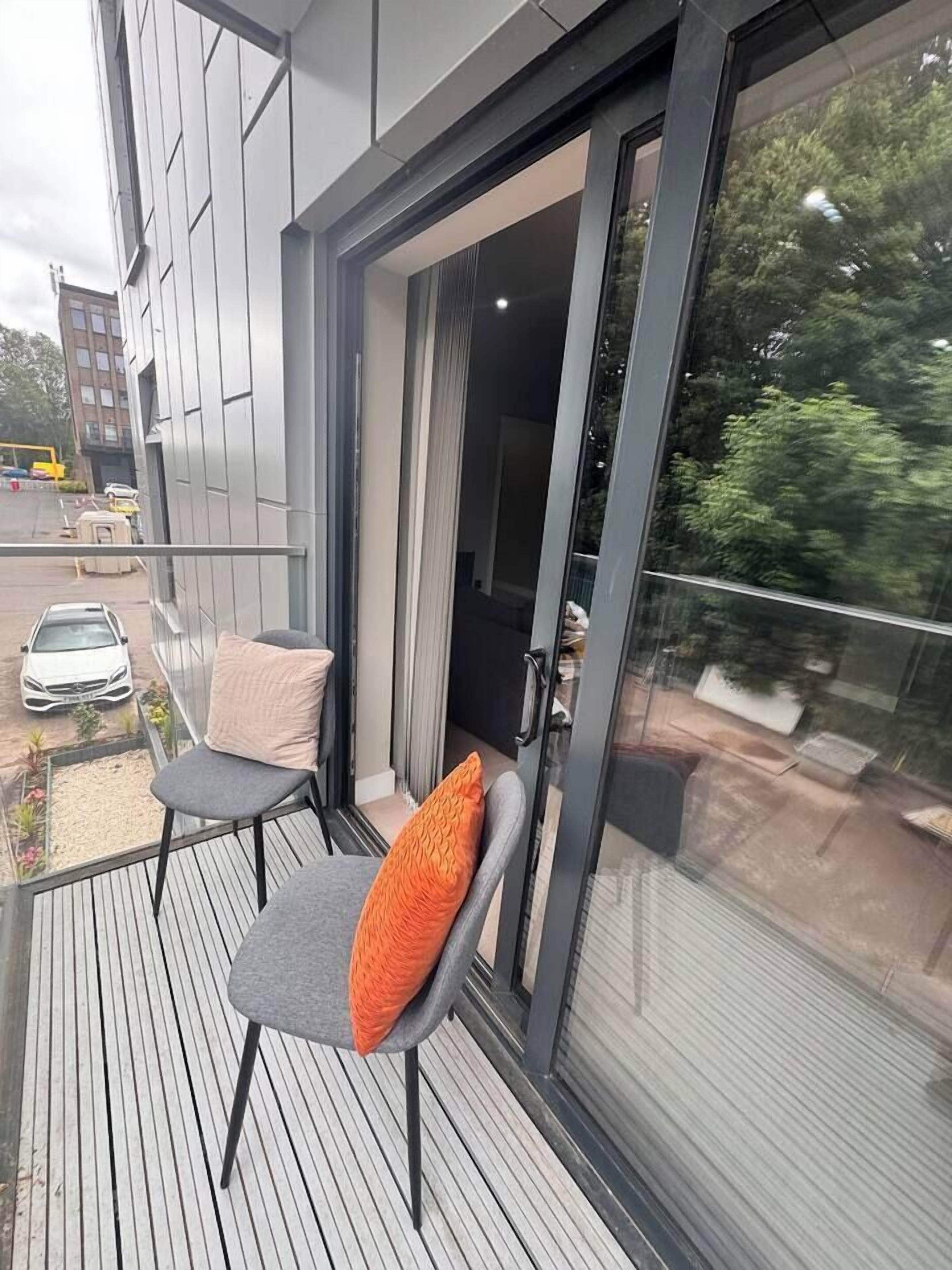 A balcony with two chairs and a glass door leading to an interior space.