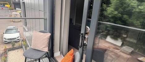 Un balcón con dos sillas y una puerta de cristal que da a un espacio interior.